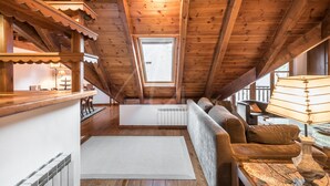 A cozy attic room with wooden beams, a sofa, a table, and a window. - Valartíes (Artíes)