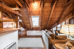 A cozy attic room with wooden beams, a sofa, a table, and a window.