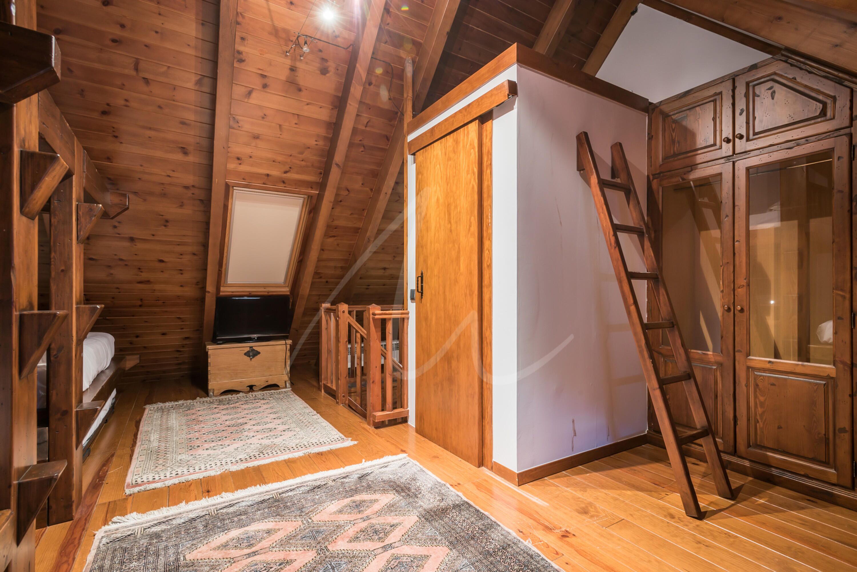 A wooden attic bedroom with a loft bed, a wooden wardrobe, and a ladder.