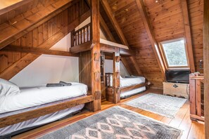 A loft bedroom with two wooden bunk beds, a skylight, and a television on a wooden dresser.