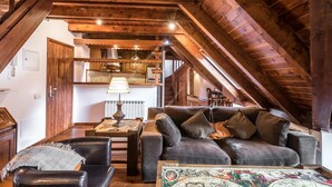 A cozy loft-style living area with a high ceiling, wooden beams, a sofa set, and a dining table. - Valartíes (Artíes)