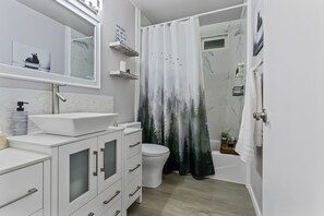 Ein modernes Badezimmer mit einem weißen Waschbecken, einem Spiegel, einem Schrank, einer Toilette und einer Duschvorhang mit Waldmuster.
