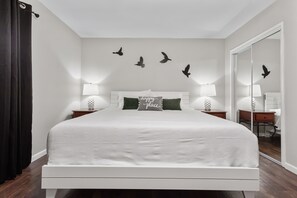 Ein modernes Schlafzimmer mit einem großen Bett, zwei Nachttischen mit Lampen, einem Spiegel und einer Wand mit Vogel-Silhouetten.
