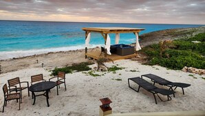 Un espace de détente aménagé sur la plage, avec un gazebo en bois, des chaises longues et une table.