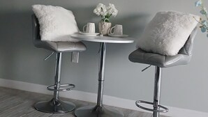 Une pièce moderne avec deux tabourets de bar, une petite table ornée d’un vase de fleurs et une horloge murale.