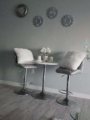 Relax in a serene space with a small table and stools, a vase with flowers, and modern wall decor.