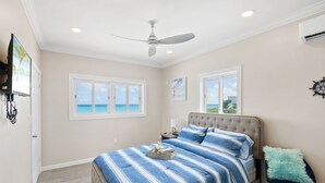 Une chambre avec un grand lit, un ventilateur de plafond et une vue sur l’océan par la fenêtre.