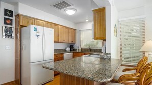 Cozinha compacta com armários de madeira, geladeira branca, bancadas de granito e uma ilha planejada com assentos.