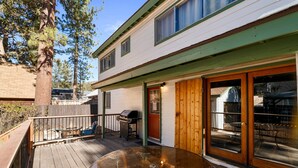 A deck with a glass-top table, a barbecue grill, and a covered patio area.