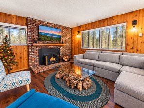 A living room with a fireplace, a sofa, a glass coffee table, and a Christmas tree. - Knotty Hideawa - Foosball, Fireplace, Deck, Fire Pit, BBQ (Big Bear City)