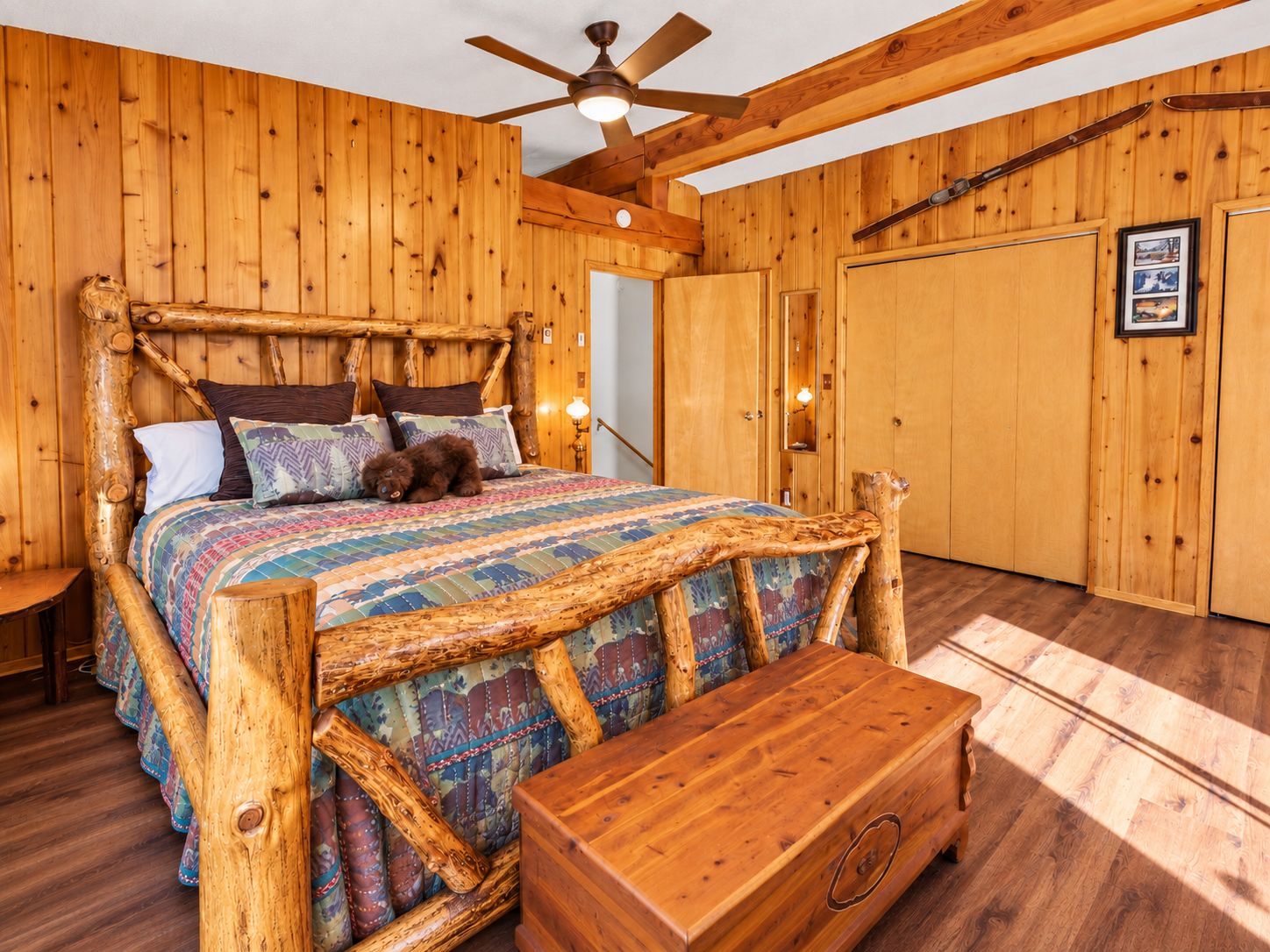 A wooden-themed bedroom with a bed, a wooden bench, and a ceiling fan.