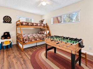 A room with a bunk bed, a foosball table, a dartboard, and a window with blinds. - Knotty Hideawa - Foosball, Fireplace, Deck, Fire Pit, BBQ (Big Bear City)