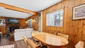 A wooden-paneled room with a fireplace, a large wooden dining table, and a sofa.