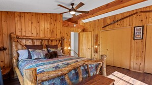 A rustic wooden bedroom with a large bed, a wooden bench, a ceiling fan, and wooden walls.