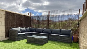 Ein Ecksofa mit Kissen, ein Couchtisch und ein Bambuszaun in einem Hinterhof mit künstlichem Rasen.