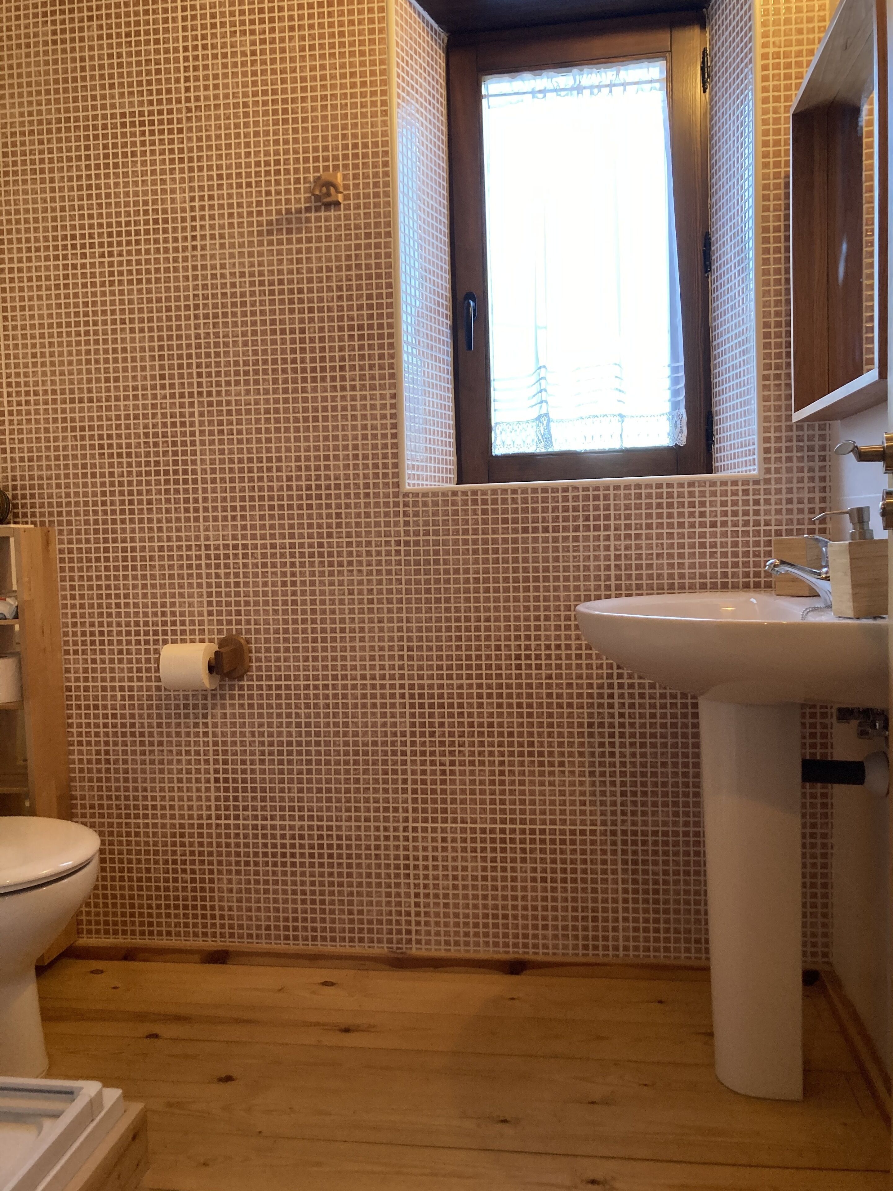 Un baño con pared de azulejos, una ventana, un inodoro y un lavabo.