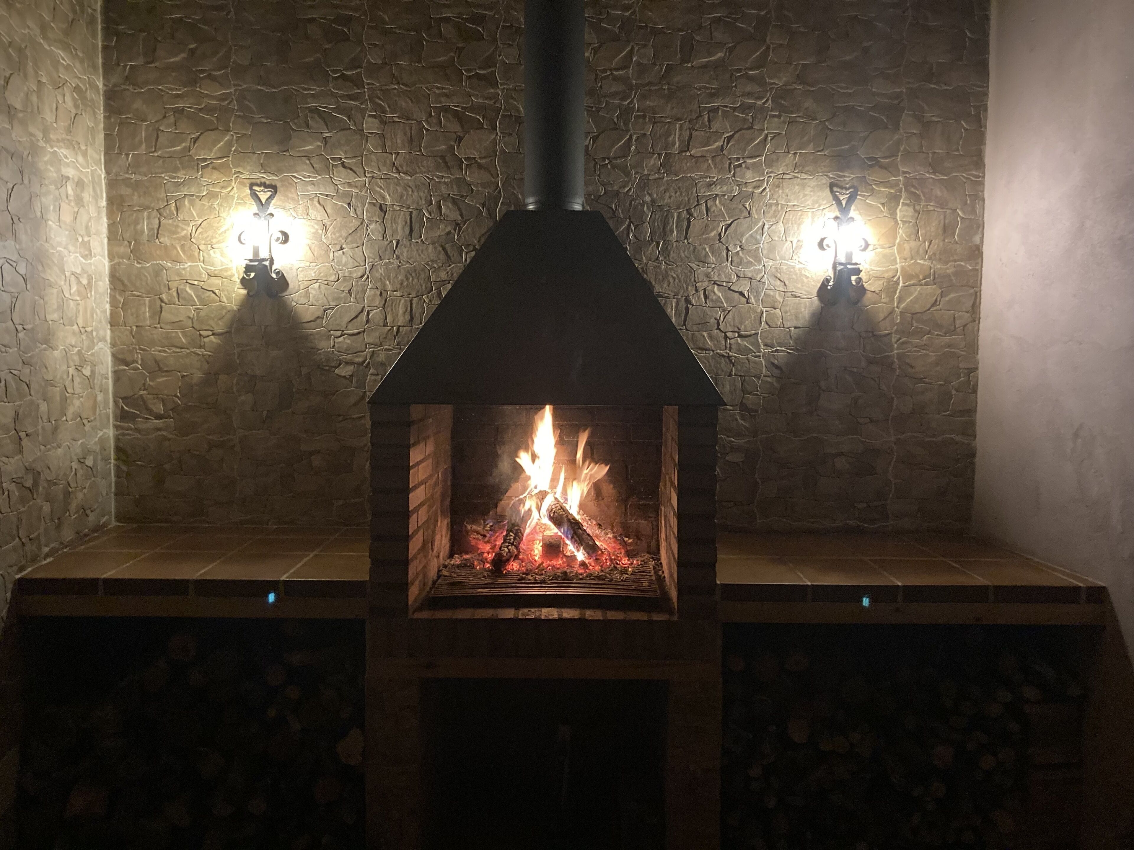 A stone fireplace with a black chimney, flanked by two wall-mounted lights.