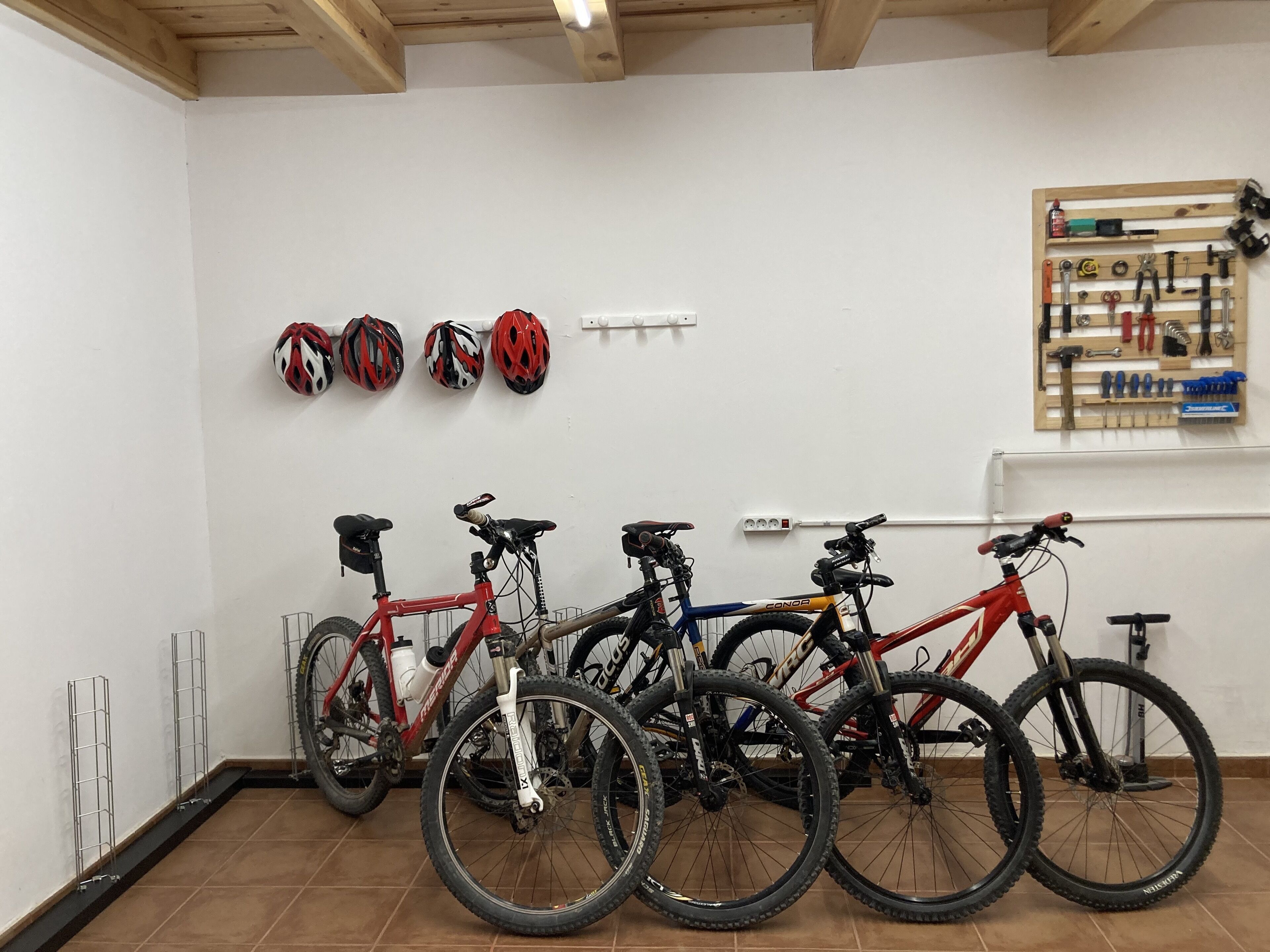 A room with bicycles and helmets on the wall, a tool rack, and a power outlet.