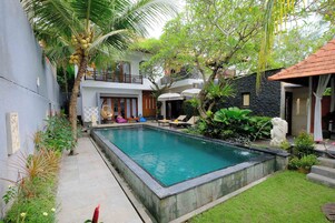 Una piscina con borde de piedra, rodeada de abundante vegetación y un pequeño jardín.