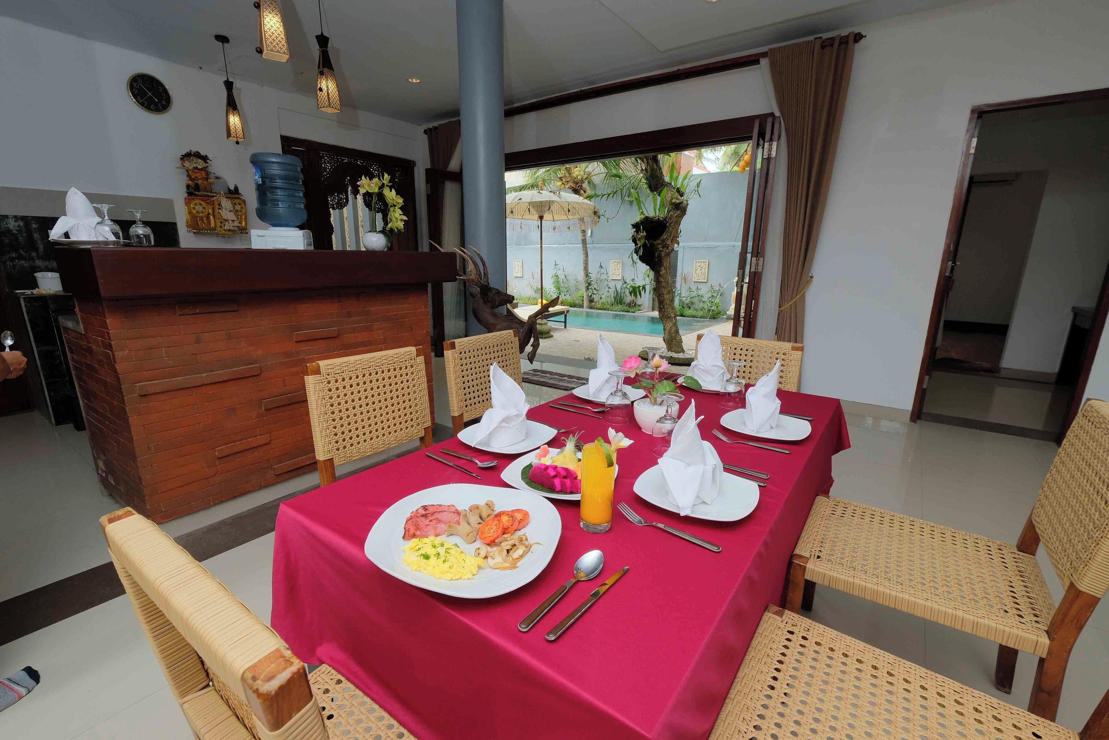 A dining area with a red tablecloth, wicker chairs, and a buffet counter with various items.
