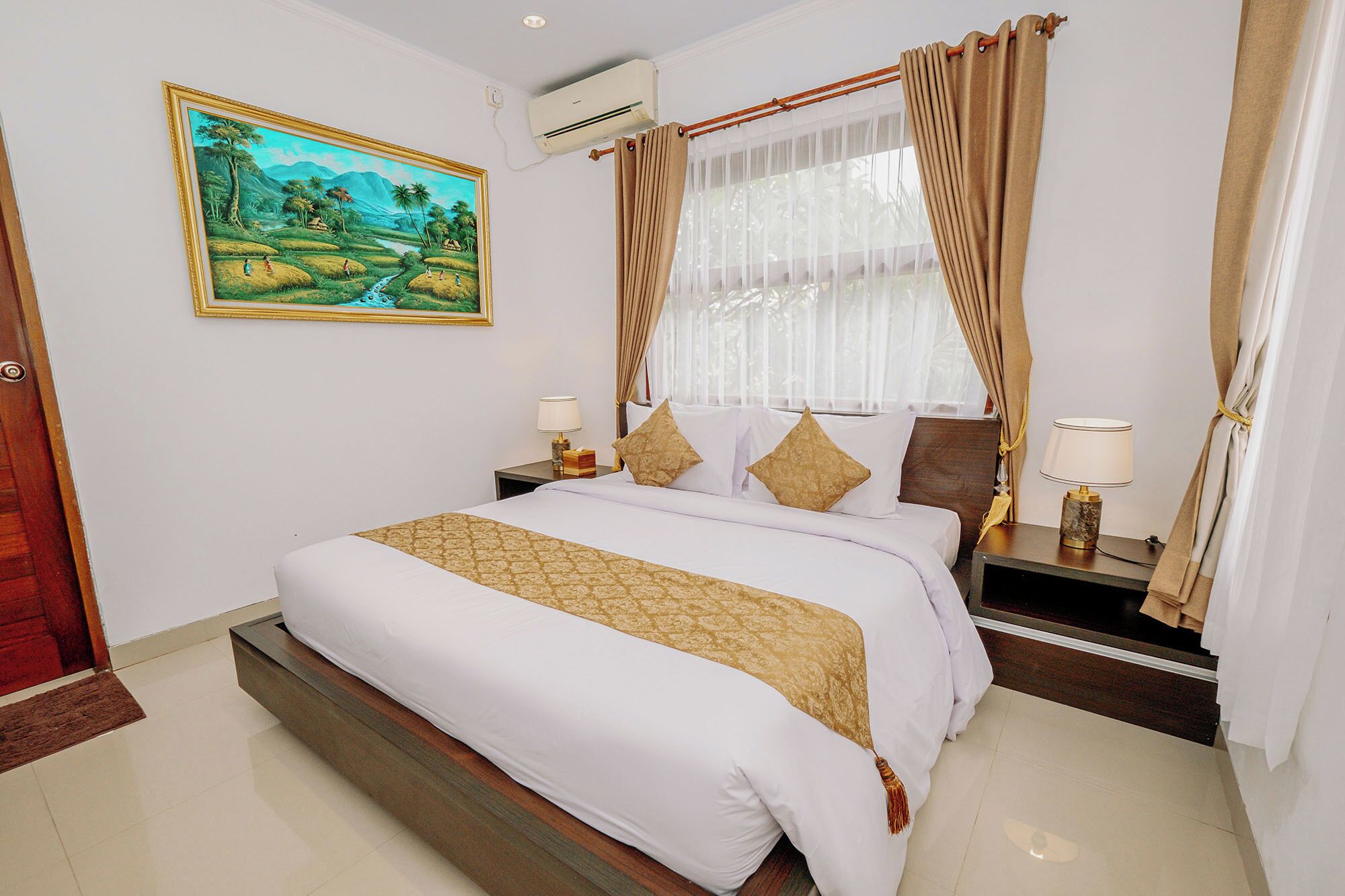 A neatly arranged bedroom with a large bed, two bedside tables with lamps, a painting on the wall, and a window with curtains.