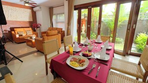 Un comedor con una mesa dispuesta para dos personas, que incluye un mantel rojo, platos de comida y cubiertos.