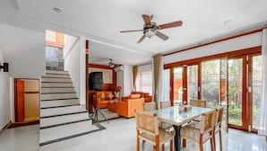 Una sala de estar moderna con comedor, una escalera y un ventilador de techo.