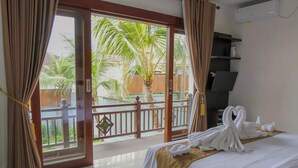 Habitación de hotel con cama, balcón y vista a palmeras, además de aire acondicionado instalado.