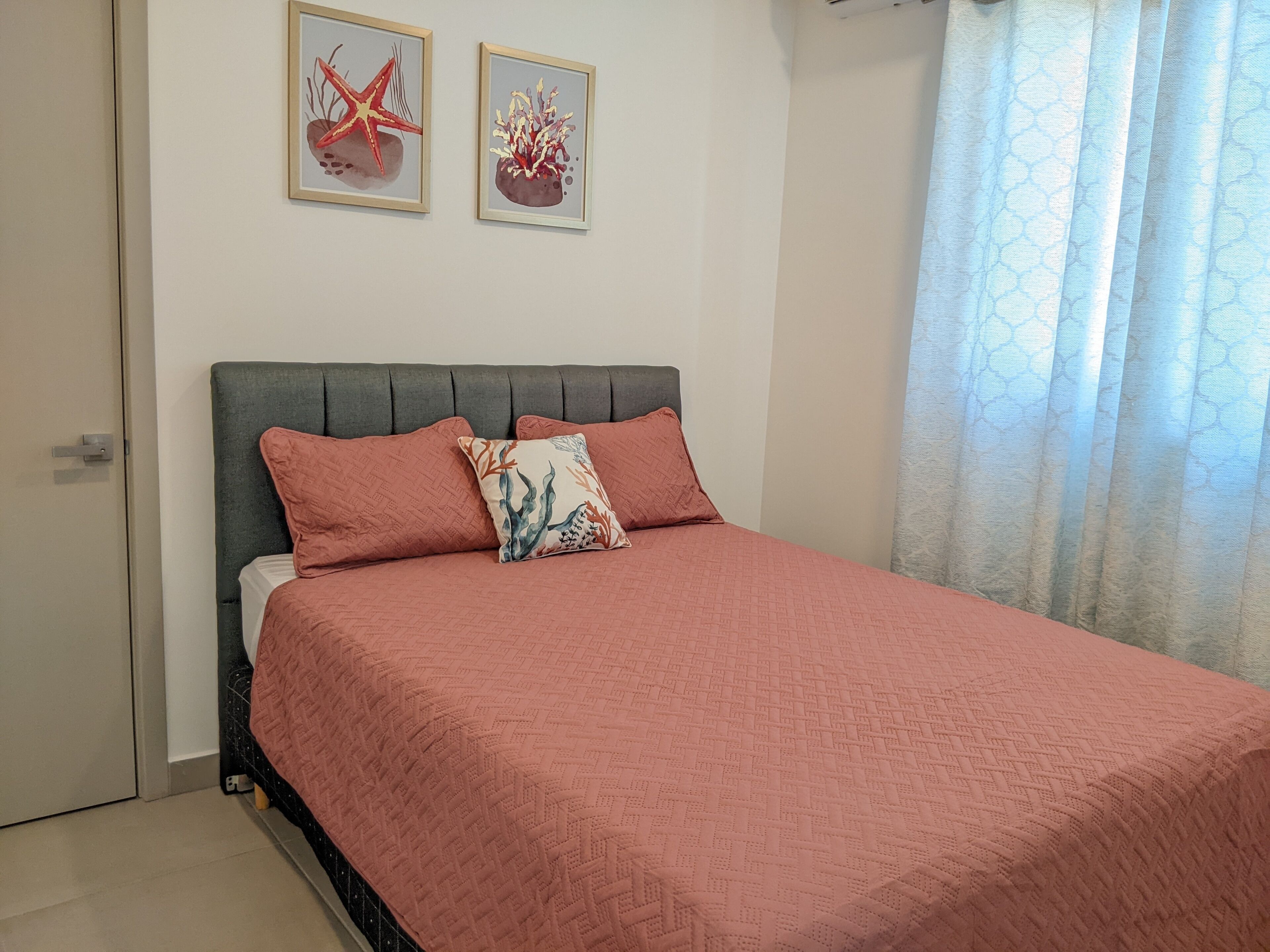 A bedroom with a bed, two wall-mounted pictures, and a window with curtains.