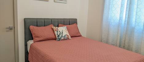 A bedroom with a bed, two wall-mounted pictures, and a window with curtains.