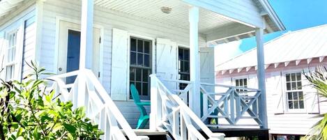 A white wooden house with a porch, steps, and a small garden.