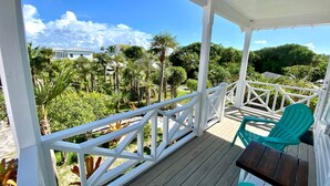 A covered outdoor area with a wooden deck, white railings, and green chairs. - Cottages on most stunning pink sand beach (North Palmetto Point)