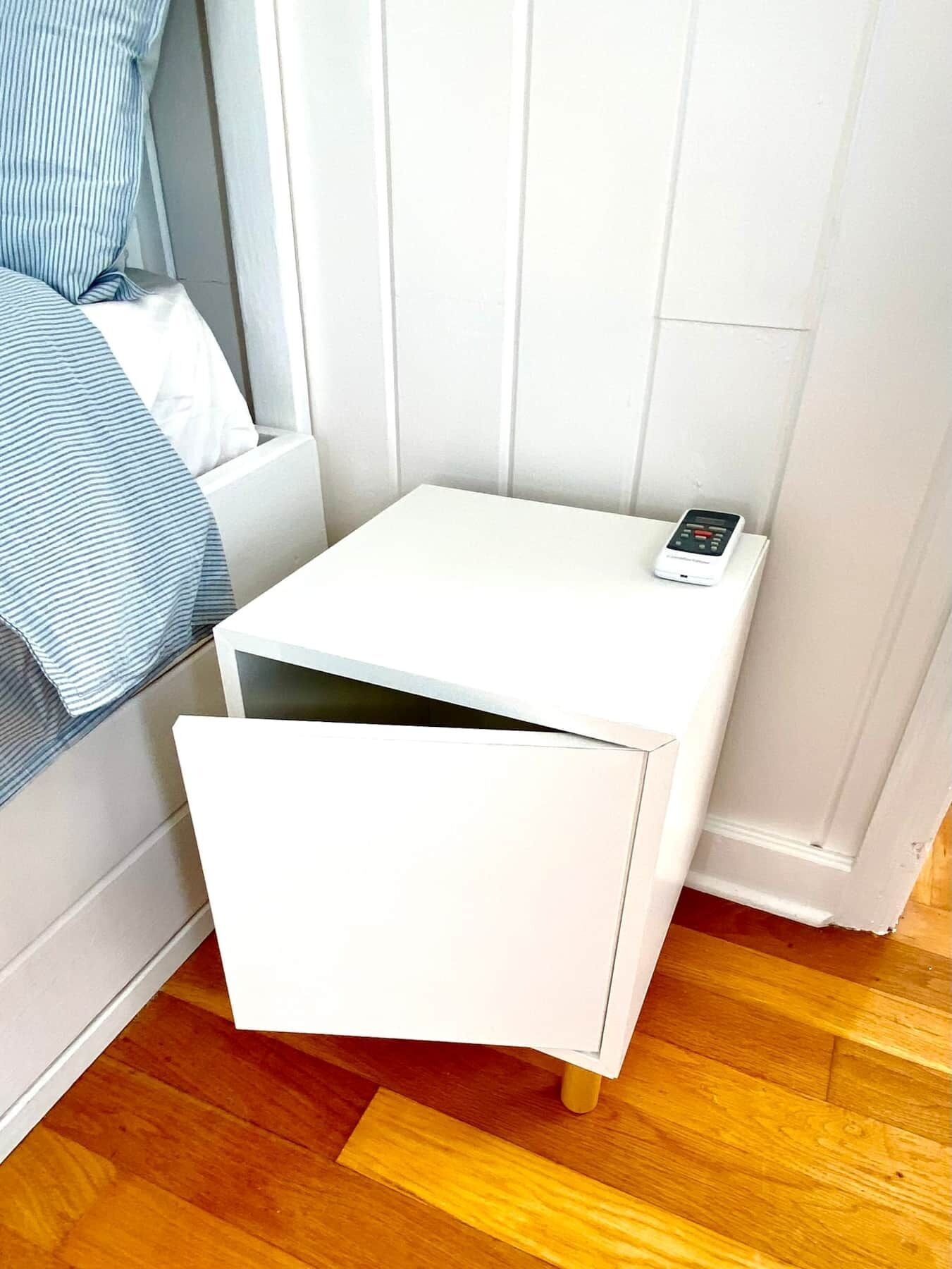 A small white bedside table with a drawer and a digital clock.