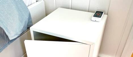 A small white bedside table with a drawer and a digital clock.