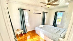 A bedroom with a bed, a small table, and a ceiling fan. - Cottages on most stunning pink sand beach (North Palmetto Point)