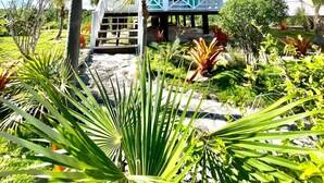 A white house with a balcony, surrounded by tropical plants and a clear blue sky. - Cottages on most stunning pink sand beach (North Palmetto Point)