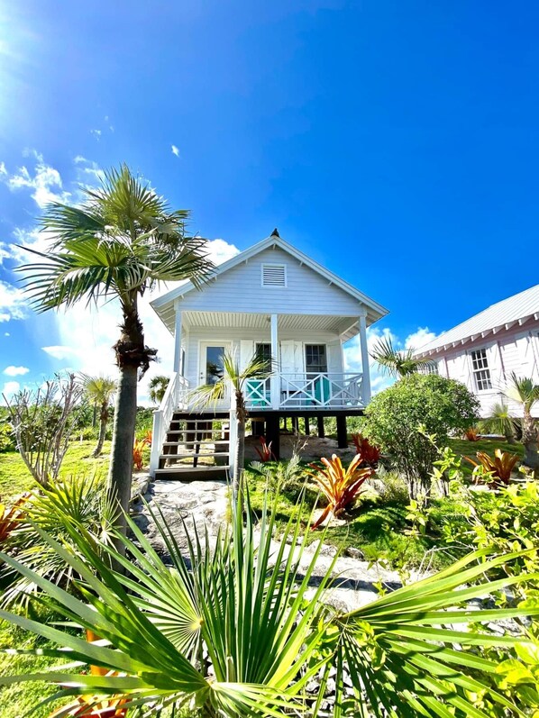 A white house with a balcony, surrounded by tropical plants and a clear blue sky.