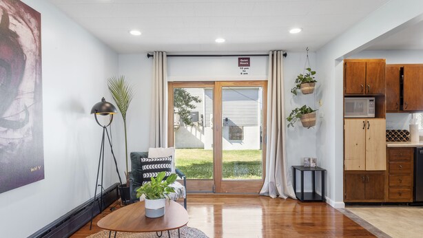 A modern interior with a wooden floor, a round table with a plant, a black lamp, and a sign indicating quiet hours. - 5BD/3BA Ranch with Vaulted Ceilings in Heart of AC (Atlantic City)
