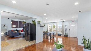 A spacious living area with hardwood flooring, a dining table, and a kitchen area with a refrigerator. - 5BD/3BA Ranch with Vaulted Ceilings in Heart of AC (Atlantic City)