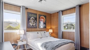A bedroom with a large bed, a bedside table, a chair, and a desk. There are two posters on the wall and a window with curtains. - 5BD/3BA Ranch with Vaulted Ceilings in Heart of AC (Atlantic City)