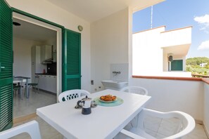 Un balcon avec une table blanche, des chaises et une assiette de pâtisseries.