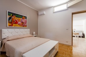 A bedroom with a bed, a painting, an air conditioning unit, and a view into another room. - 2904 Residence Mareluna - Bilo 2 by Barbarhouse (Porto Cesareo)