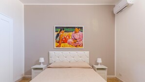 A bedroom with a bed, two bedside tables with lamps, a wall-mounted air conditioner, and a painting above the bed. - 2904 Residence Mareluna - Bilo 2 by Barbarhouse (Porto Cesareo)