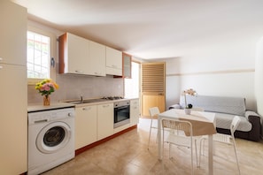 A compact kitchen with a washing machine, stove, oven, and a dining area with a table and chairs.