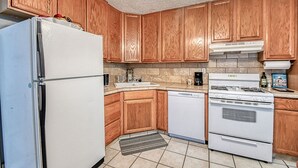 Una cocina con armarios de madera, un refrigerador blanco, un lavavajillas, una estufa y un fregadero.