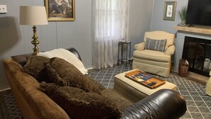 Una sala de estar con sofá, sillón, reposapiés, chimenea, televisor y un cuadro en la pared.