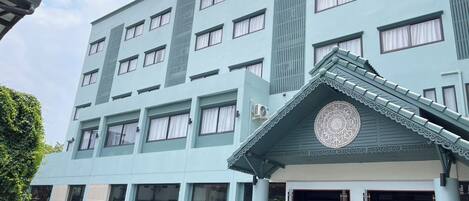 Un hotel de varios pisos con fachada azul claro, ventanas amplias y una entrada decorativa con un diseño circular.