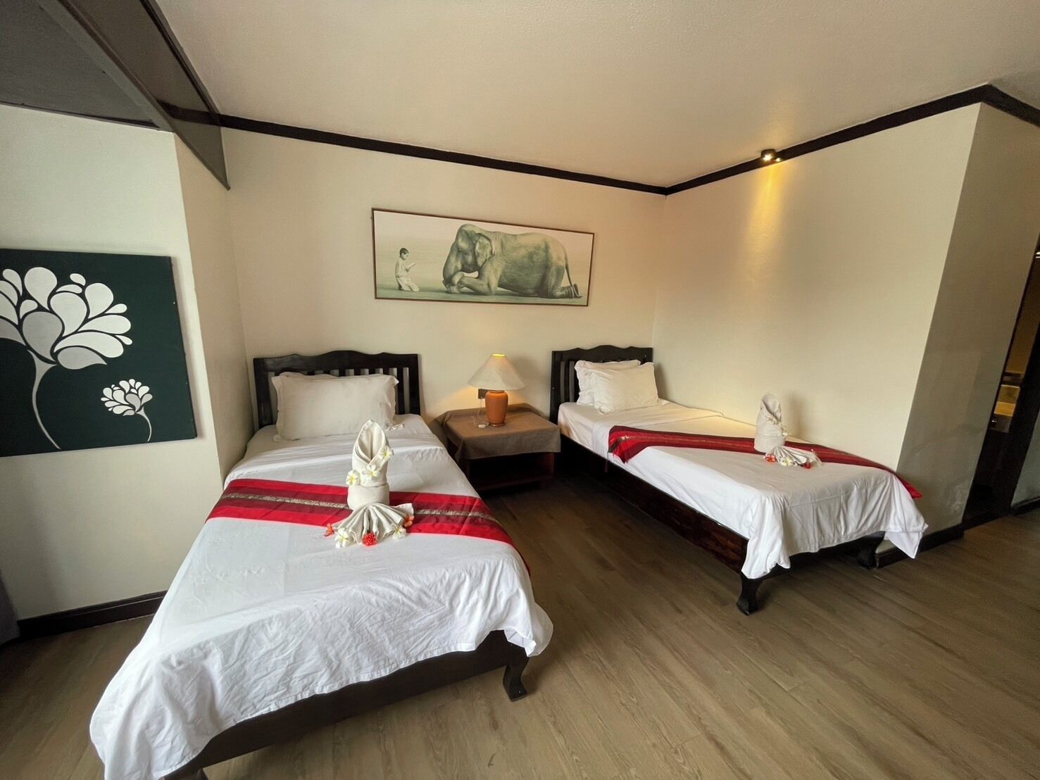 Een hotelkamer met twee bedden, een nachtkastje, een lamp en een schilderij aan de muur.
