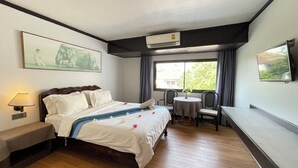 Quarto de hotel com cama, mesa de cabeceira, luminária, ar condicionado, janela com cortinas e televisão.