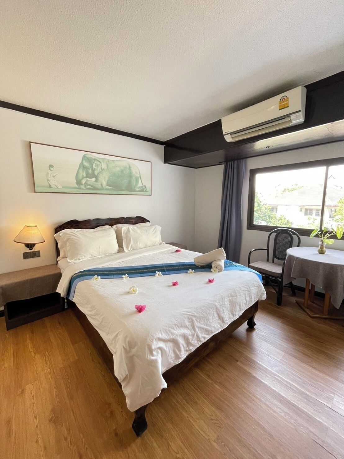 Una habitación de hotel con cama, lámpara de noche, ventana y aire acondicionado instalado en la pared.